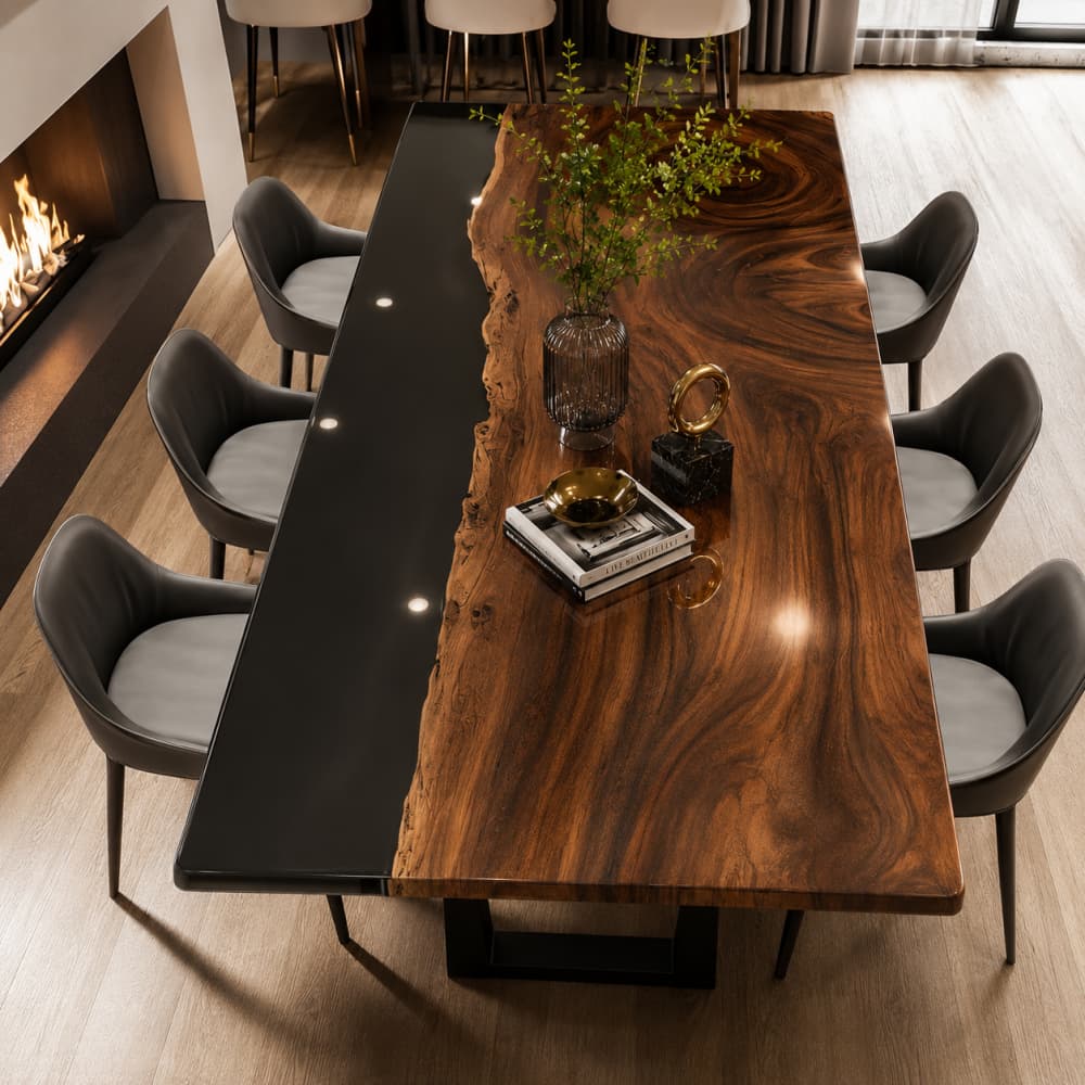 Diagonal full lifestyle shot of asymmetrical live edge walnut dining table with reflective mirror black epoxy river strip, surrounded by curved grey leather dining chairs beside lit modern fireplace in high-end residential dining room with floor-to-ceiling window curtains