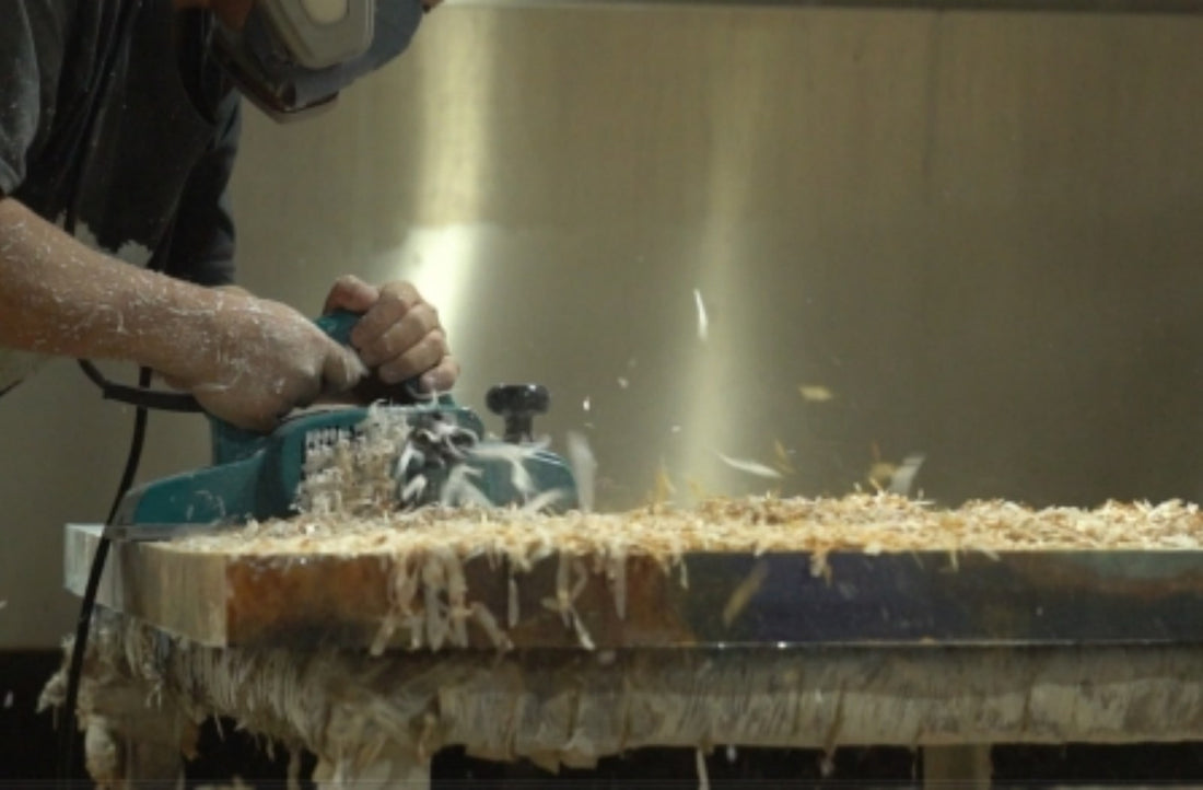Woodworker sanding surface of large live‑edge walnut slab in workshop, wood shavings on workbench