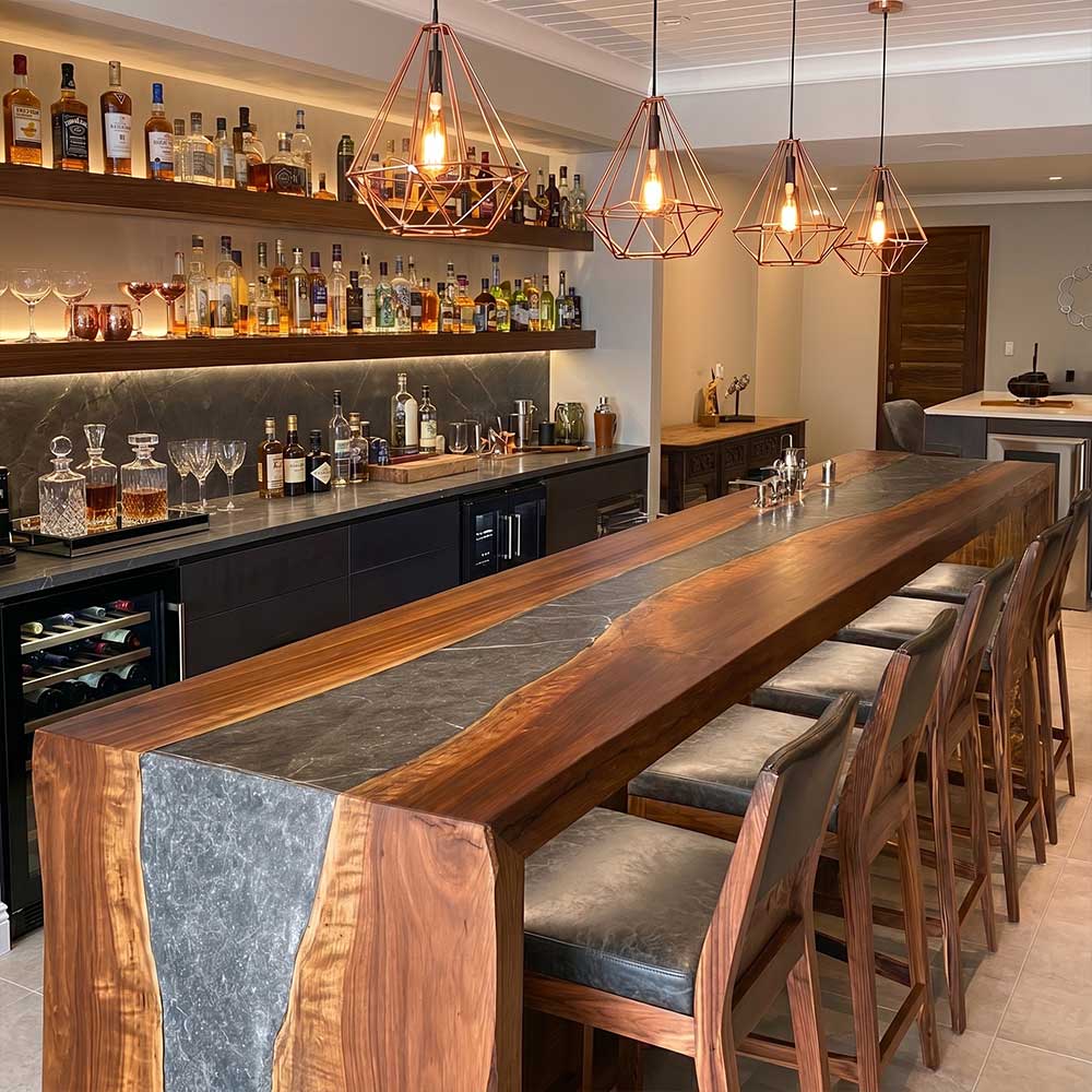 Modern bar with wooden counter, stools, and shelves stocked with drinks.