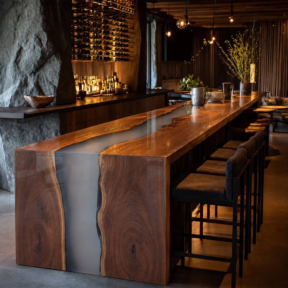 Premium custom walnut waterfall bar table featuring a gray resin river inside a dark moody home lounge with barstools